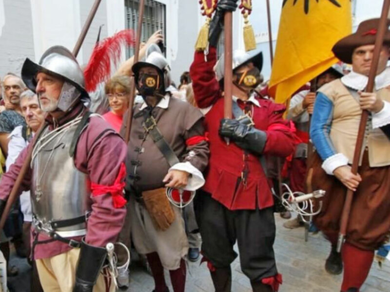 Recreación histórica de soldados del siglo XVI con armaduras y banderas en una calle urbana.