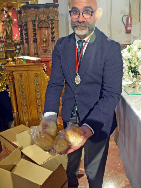 Un hombre en traje sostiene una caja de pan en una iglesia con un altar decorado.
