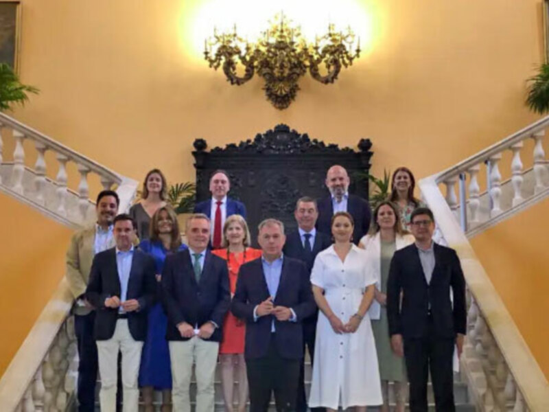Grupo de personas posando en una escalera con decoración clásica en el fondo.