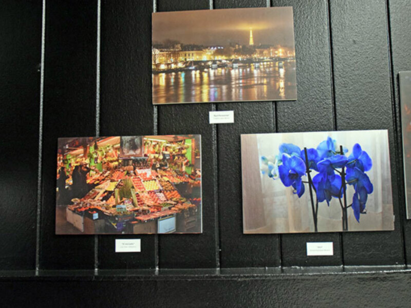 Una exposición de fotos en una pared de azulejos, con una imagen nocturna de la Torre Eiffel y otra de flores azules en el centro.