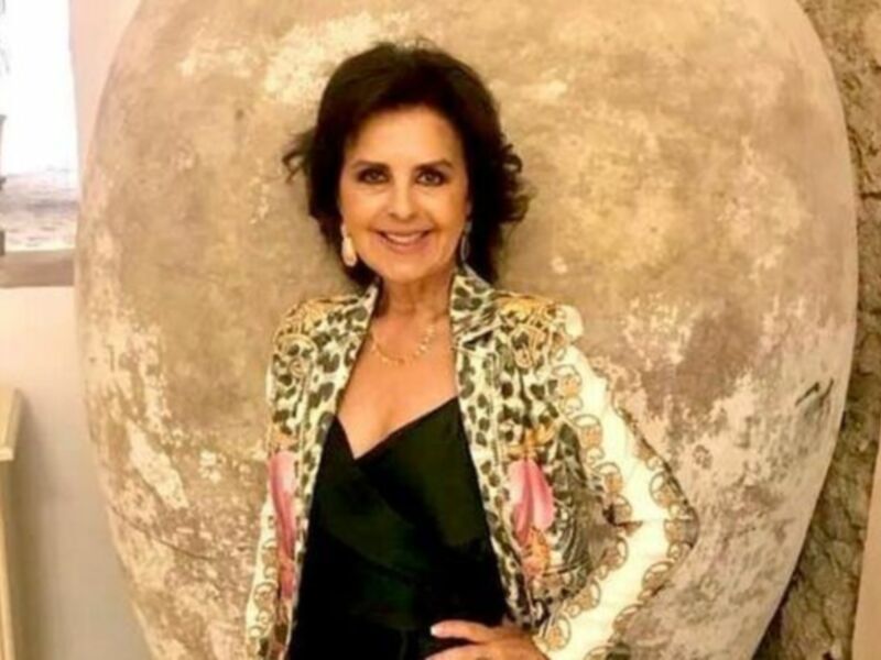 Retrato de una mujer sonriente con chaqueta de leopardo y vestido negro, posando frente a una decoración de huevo gigante.