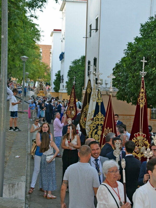 Procesión religiosa con portadores de estandartes y devotos en una calle urbana.