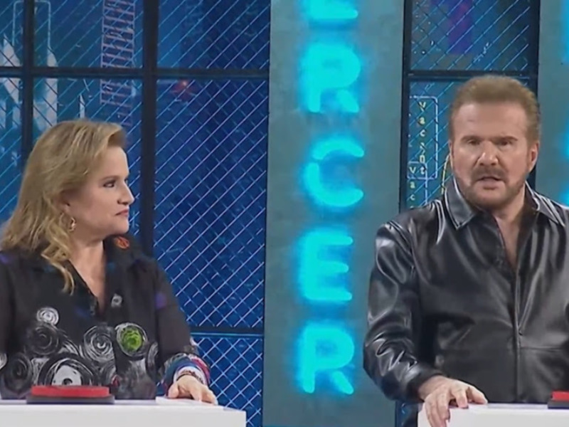 Dos personas en un set de televisión con un fondo azul y letras en el aire.