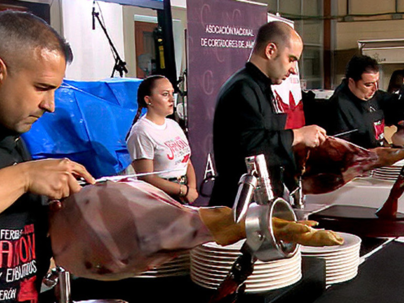 Corte de jamón en un evento gastronómico, con personas ayudando a cortar y servir el producto.