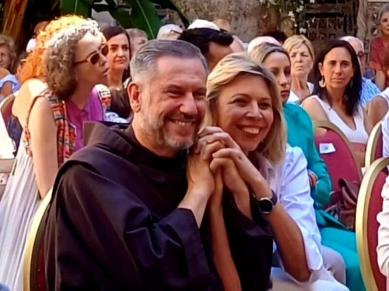 Un hombre y una mujer sonrientes en un evento público, rodeados de una audiencia atenta.