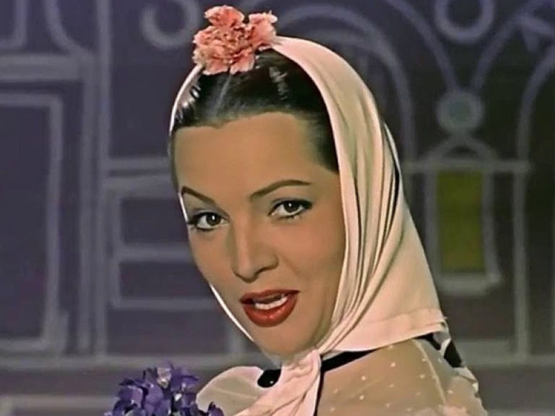 Retrato de mujer con pañuelo rosa y flores, fondo arquitectónico.