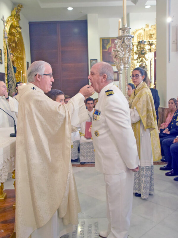 Un clérigo y un oficial militar en uniforme blanco participan en una ceremonia religiosa en una iglesia.