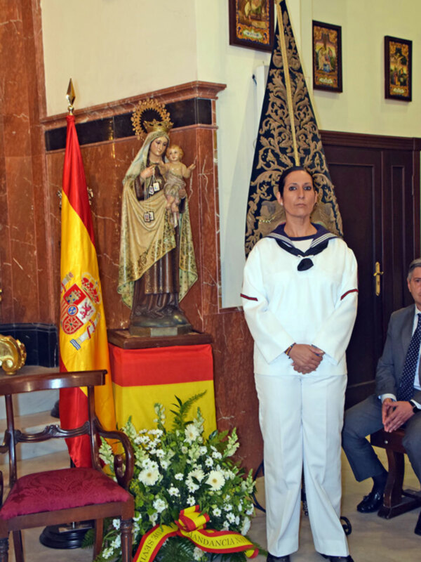 Celebración con bandera española y estatua de la Virgen del Carmen en un ambiente solemne.