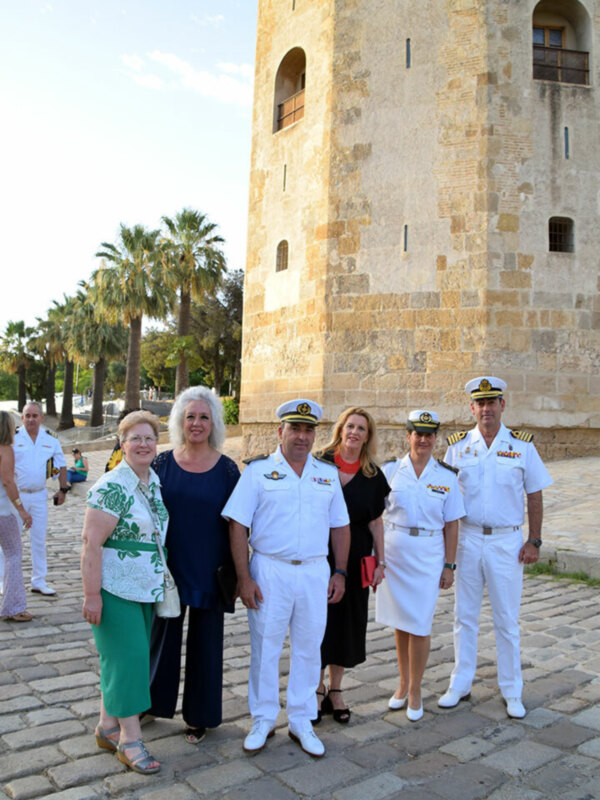 Una familia en uniforme militar posa frente a una torre histórica, con palmeras y cielo azul en el fondo.