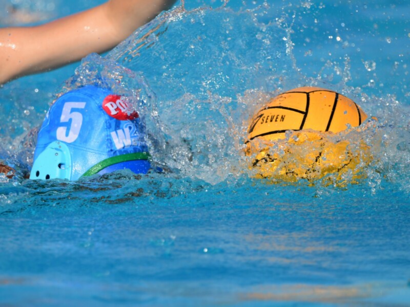Jugador de waterpolo en acción, con balón y casco en el agua.