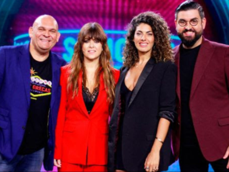 Un grupo de cuatro personas, dos hombres y dos mujeres, sonríen frente a un fondo con luces y colores vibrantes, posiblemente en un programa de televisión o evento.
