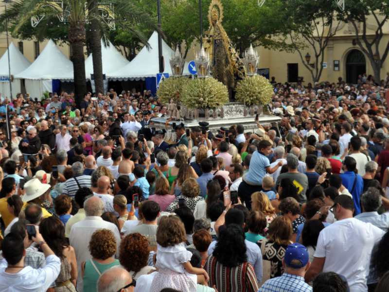 Procesión religiosa con una imagen procesional en un entorno urbano con mucha gente observando.