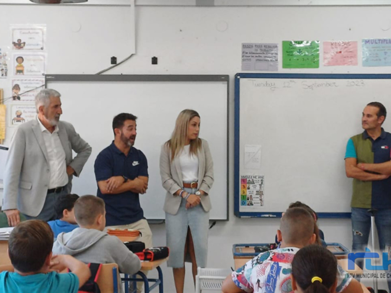 Un grupo de personas en una sala de conferencias, con una mujer en el centro y otros dos hombres a su lado. La sala está decorada con carteles y una pizarra en el fondo.
