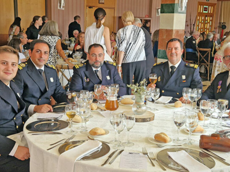 Oficiales en uniforme sentados alrededor de una mesa decorada con copas y panes, en un evento formal.
