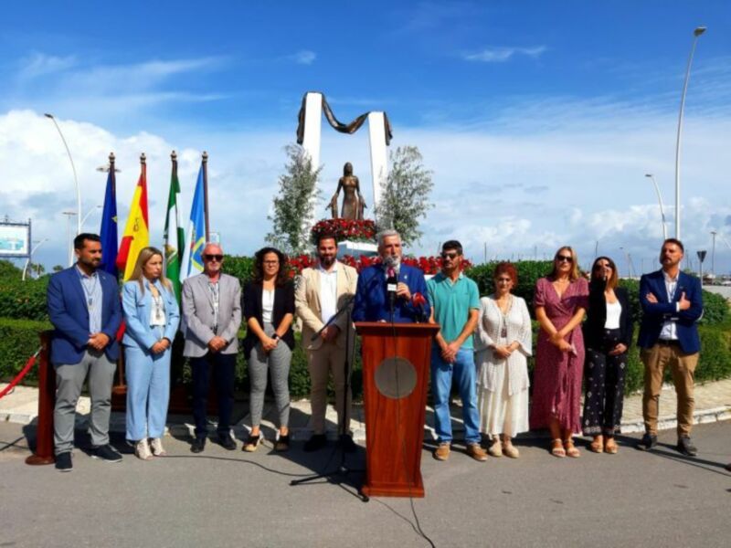 Inauguración de un monumento con una figura femenina en el centro, rodeado por una ceremonia oficial con banderas y un discurso en un podio.