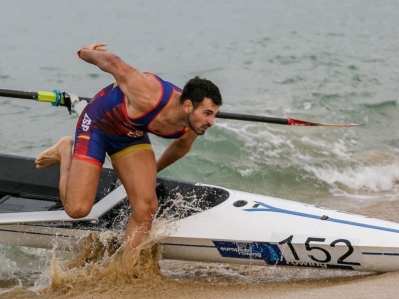 Joven nadador en acción en el agua, con una barca de remo y el número 152 visible en ella.
