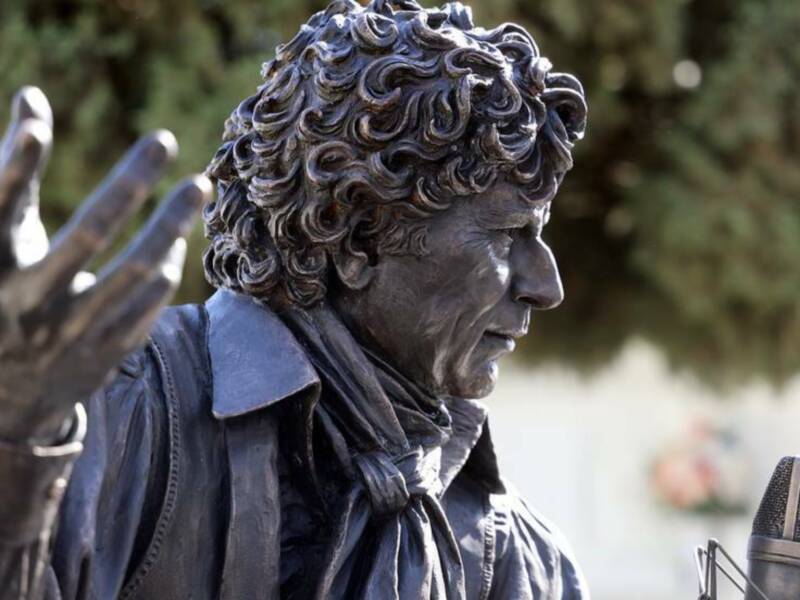 Estatua de bronce de un personaje con cabello rizado y gesto de mano levantada, posiblemente un líder o figura histórica.