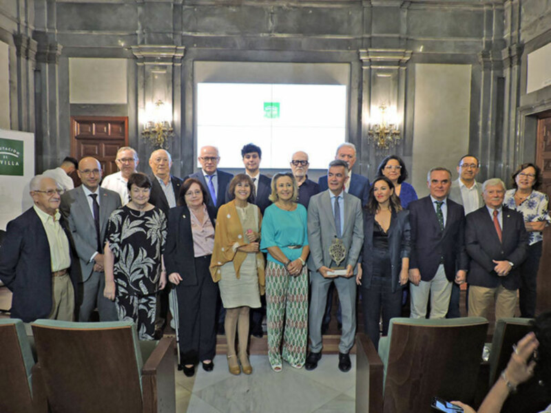 Galería de personas en una ceremonia de premiación en un salón con arcos y lámparas de pared.
