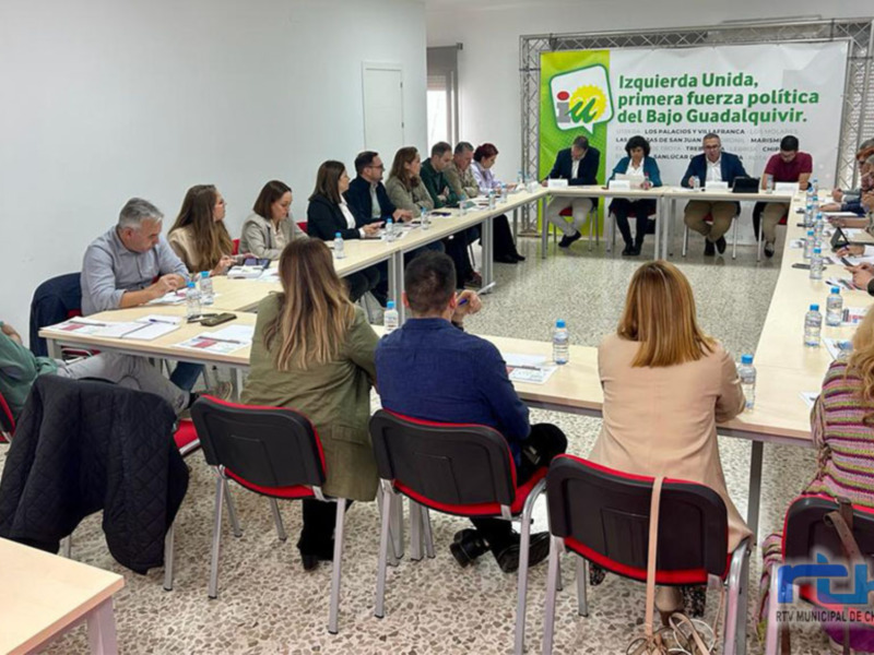 Reunión de trabajo en una sala de conferencias con una bandera de Izquierda Unida en el fondo.