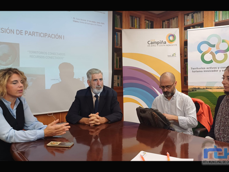 Una reunión de trabajo en un salón de conferencias con tres personas sentadas en una mesa, frente a un proyector y dos carteles con el logo de CDS Campiña y el texto 'Territorios conectados, recursos conectados'.