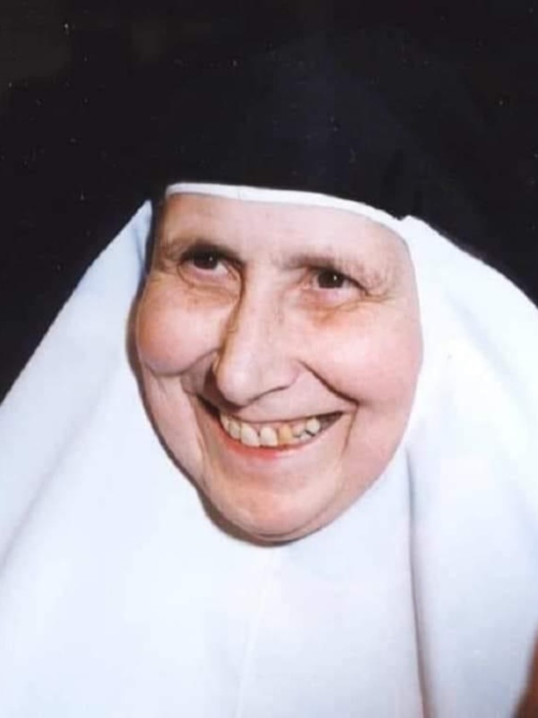 Retrato de una monja sonriente, vestida con hábito blanco y capucha negra.