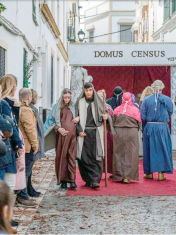 Recreación histórica en una calle de pueblo con personajes vestidos con trajes tradicionales y un letrero que dice 'DOMUS CENSUS'.