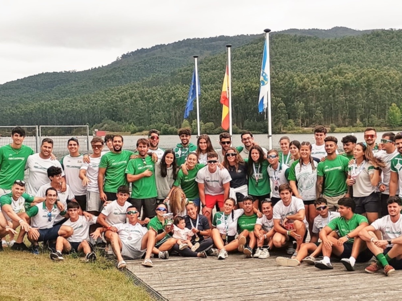 Equipo de atletas posando para la foto en el lago, con banderas nacionales en el fondo.