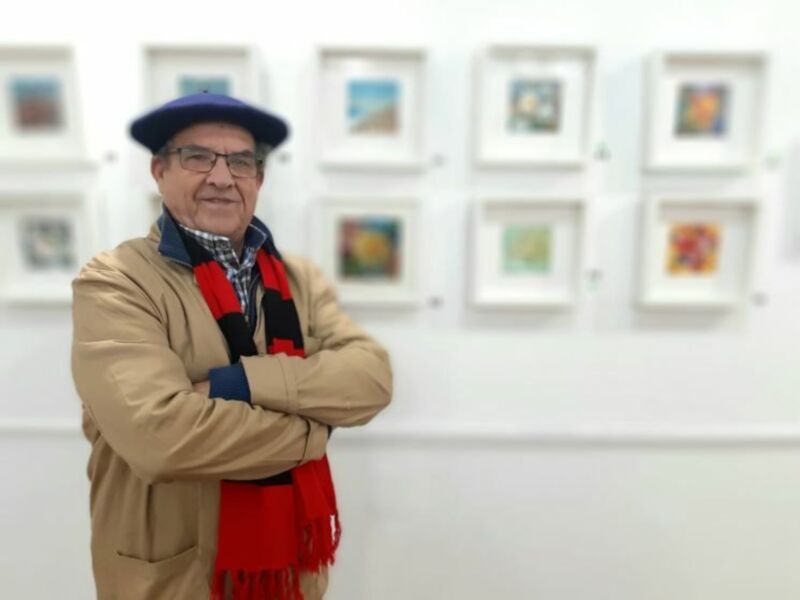 Artista en una exposición de arte, rodeado de obras de arte enmarcadas.