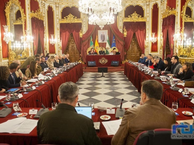 Sala de conferencias con mesas redondas, personas sentadas, decoración elegante y luces de cristal en el techo.