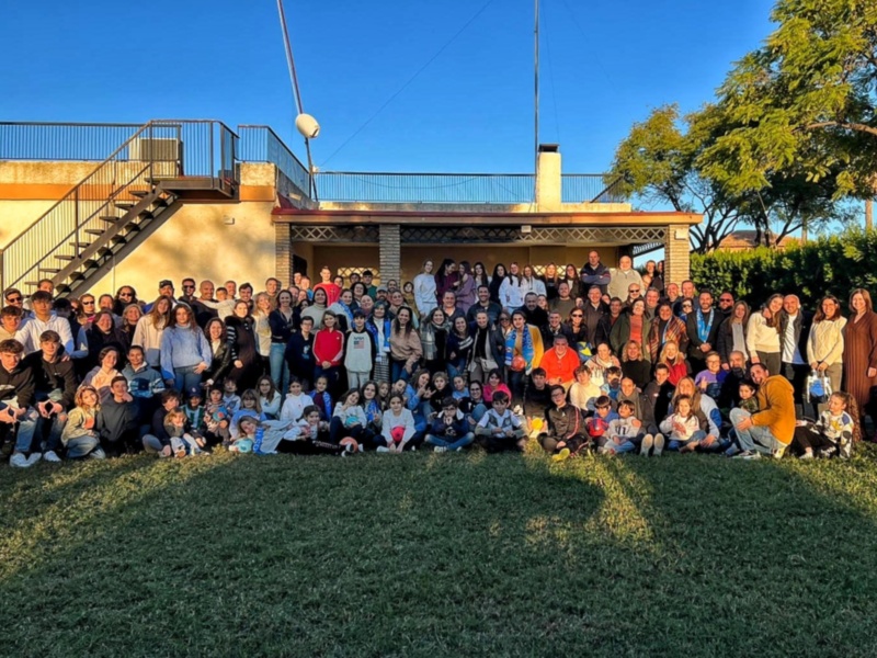 Una gran reunión de amigos y familiares en un día soleado, disfrutando de la compañía y la naturaleza al aire libre.