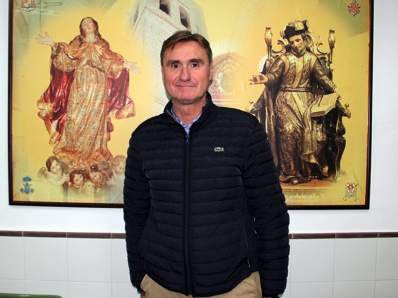 Hombre posando frente a un retrato religioso de la Virgen y San Juan Bautista.