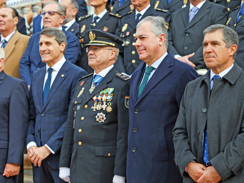 Oficiales y autoridades en una ceremonia oficial, destacando un militar con insignias y otros en trajes formales.
