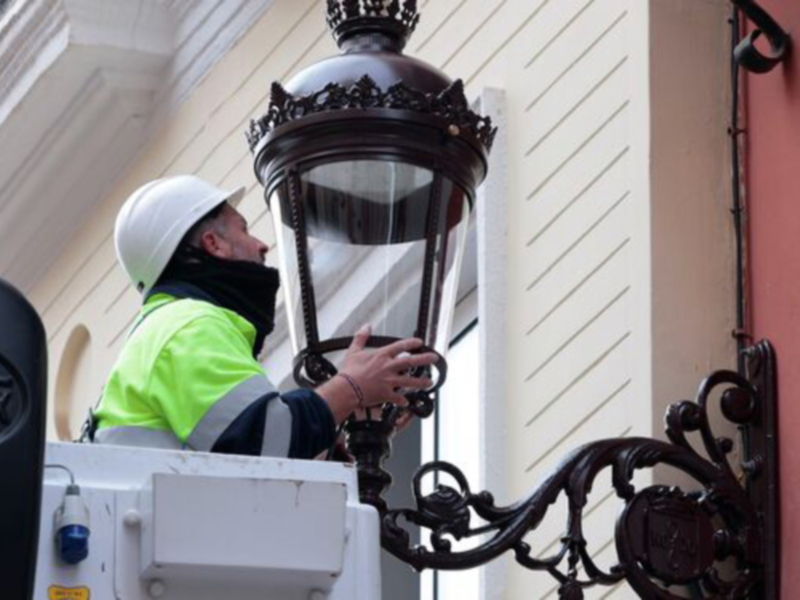 Trabajador en elevador reparando una lámpara de calle en edificio histórico.