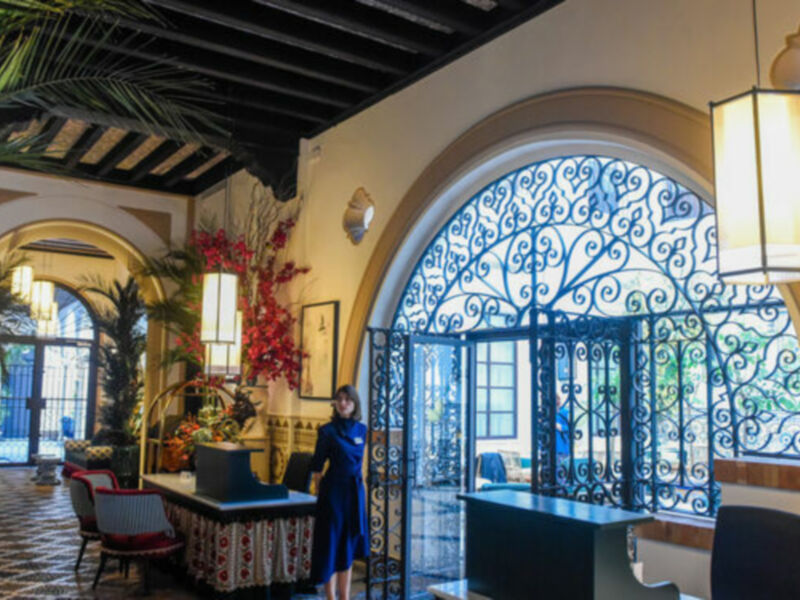 Elegante recepción de un hotel con decoración exótica y una mujer vestida con un vestido azul en el centro de la imagen.