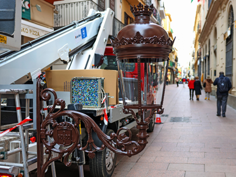 Instalación de farola ornamental en calle adoquinada con edificios históricos al fondo.