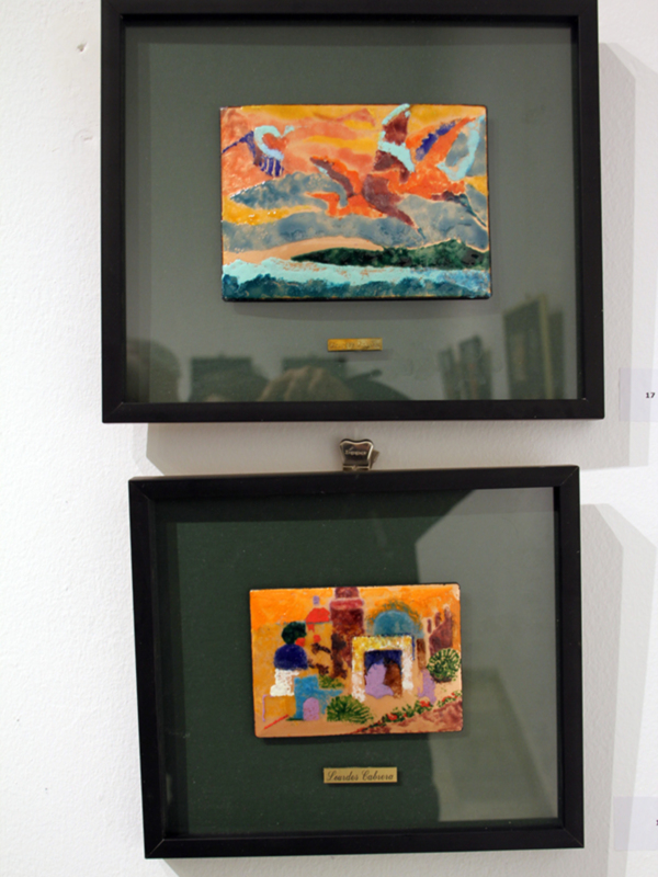 Dos cuadros enmarcados colgados en una pared, con temas de paisajes y personajes en colores vibrantes.