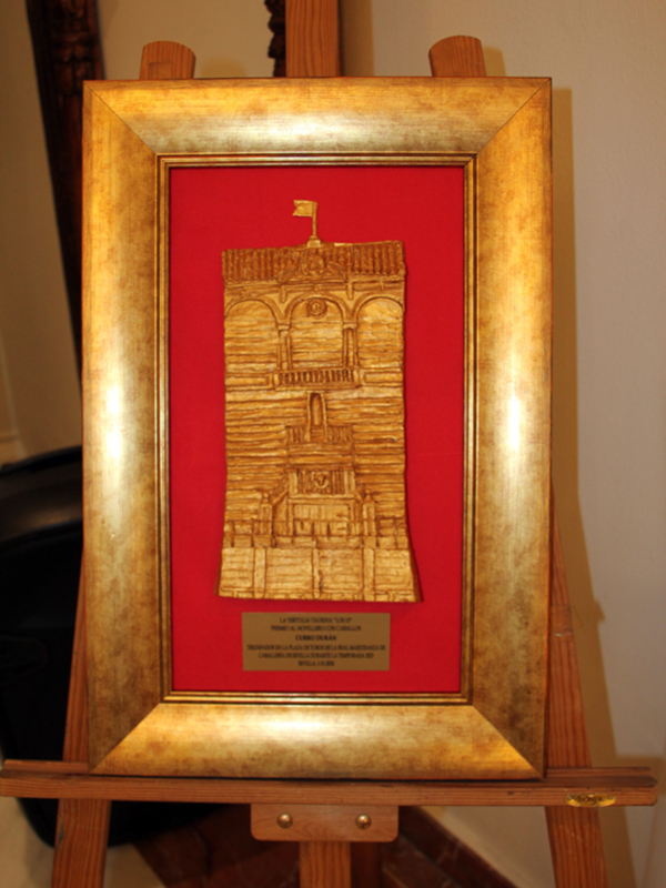 Estructura de madera con marco dorado y fondo rojo, mostrando una imagen tallada en madera de una estructura histórica.