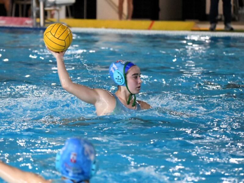 Jugadora de waterpolo en acción, sosteniendo el balón mientras nada en la piscina.