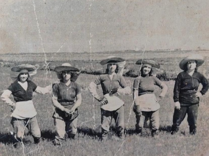 Historic image of five women standing in a field, wearing hats and aprons, likely from the early 20th century.