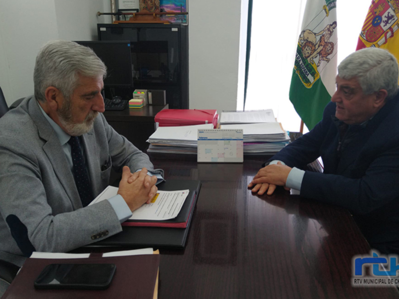 Dos hombres en una reunión formal en un escritorio, con banderas y documentos en el fondo.