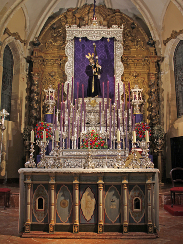 Altar con ornamentos y estandarte en una iglesia, decorado con flores y velas de color púrpura.
