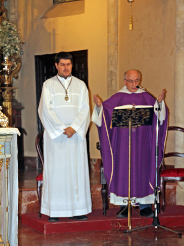 Dos sacerdotes en una ceremonia religiosa en un interior de iglesia con altares y decoración clásica.