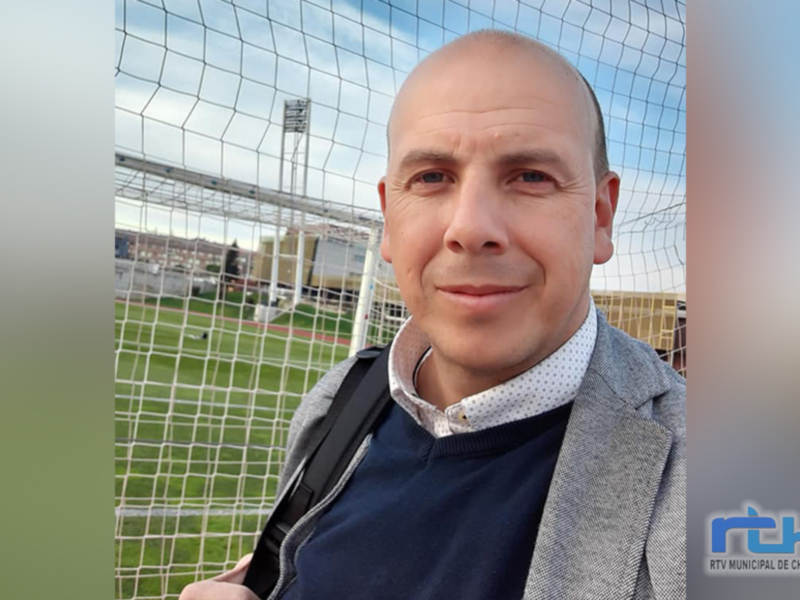 Selfie de un hombre frente a un campo de fútbol, con una red de portería en el fondo. El hombre lleva una chaqueta gris y una camisa blanca con lunares azules. La imagen está firmada con el logo de RTV Municipal de Chipiona en la parte inferior derecha.