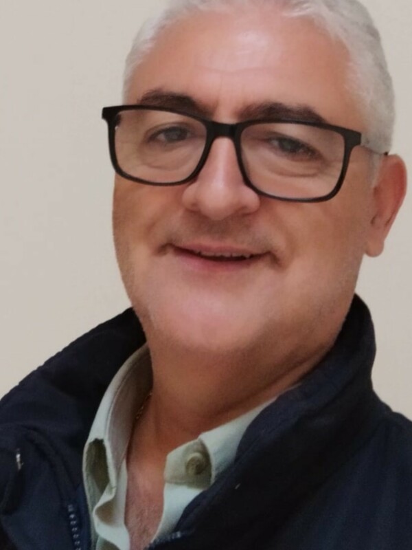 Retrato de hombre con gafas y chaqueta de color oscuro, sonriendo.