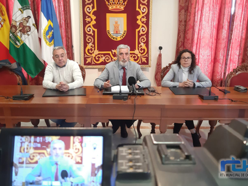 Conferencia de prensa en el Ayuntamiento de Chipiona, con representantes municipales y banderas de España y Andalucía en el fondo.