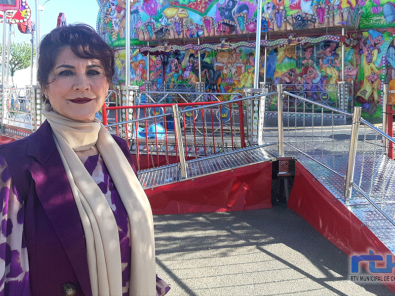 Mujer sonriente frente a un carrusel colorido en un parque de atracciones.