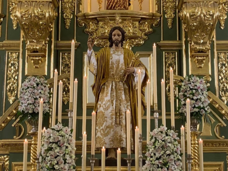 Efigie de Jesús en un altar ornado con velas y flores, en un entorno religioso con decoración barroca.