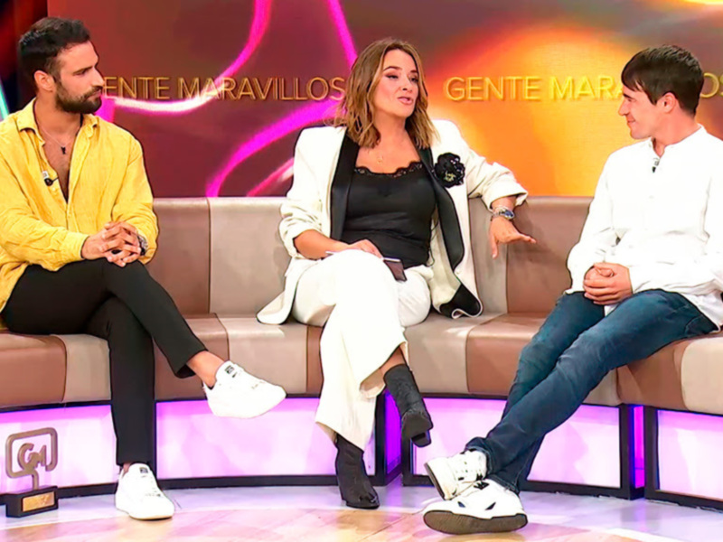 Tres personas sentadas en un sofá en un programa de televisión, con un fondo colorido y la palabra 'Gente Maravillosa' en el escenario.