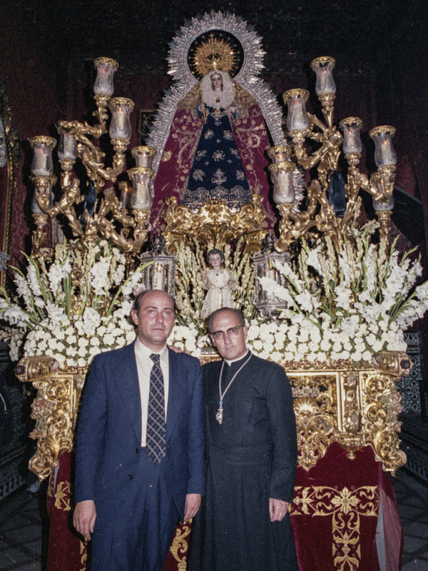 Dos personas posan junto a una imagen religiosa en un ambiente festivo.