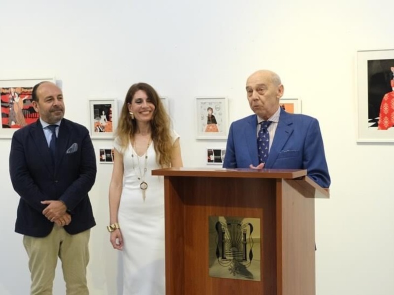 Presentación en una galería de arte con tres personas en un podio, rodeados de obras de arte enmarcadas en la pared.